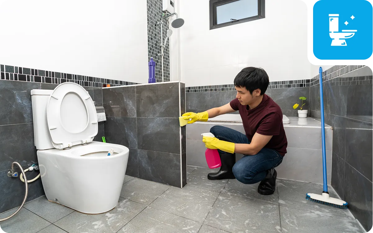 Man cleaning bathroom floor with spray bottle.